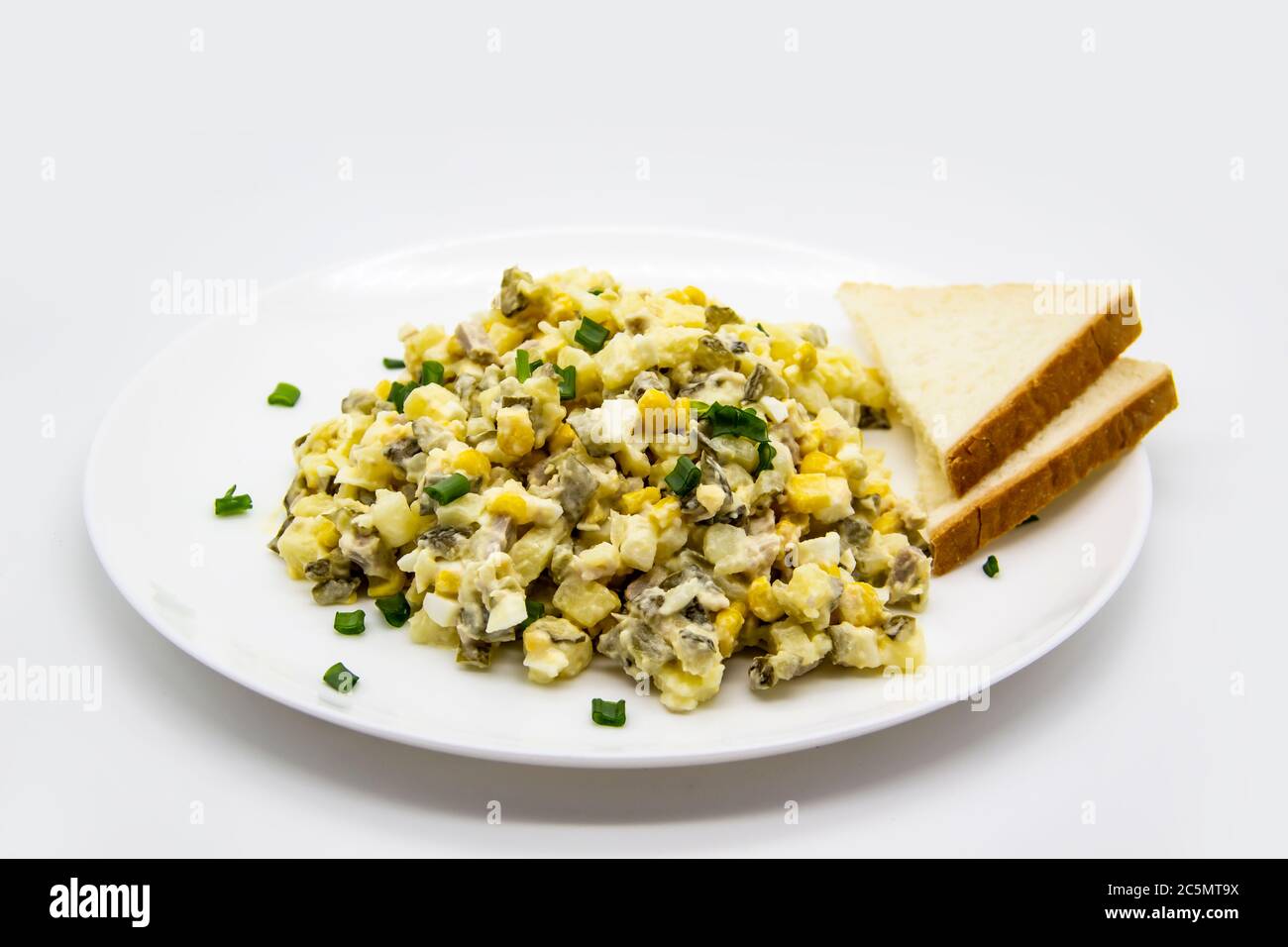 Ukrainischer und russischer Salat Olivier nach einem neuen Rezept auf einem weißen Teller. Gesunder Salat Olivier mit Fleisch, Mais und Scheiben Weißbrot. Delic Stockfoto