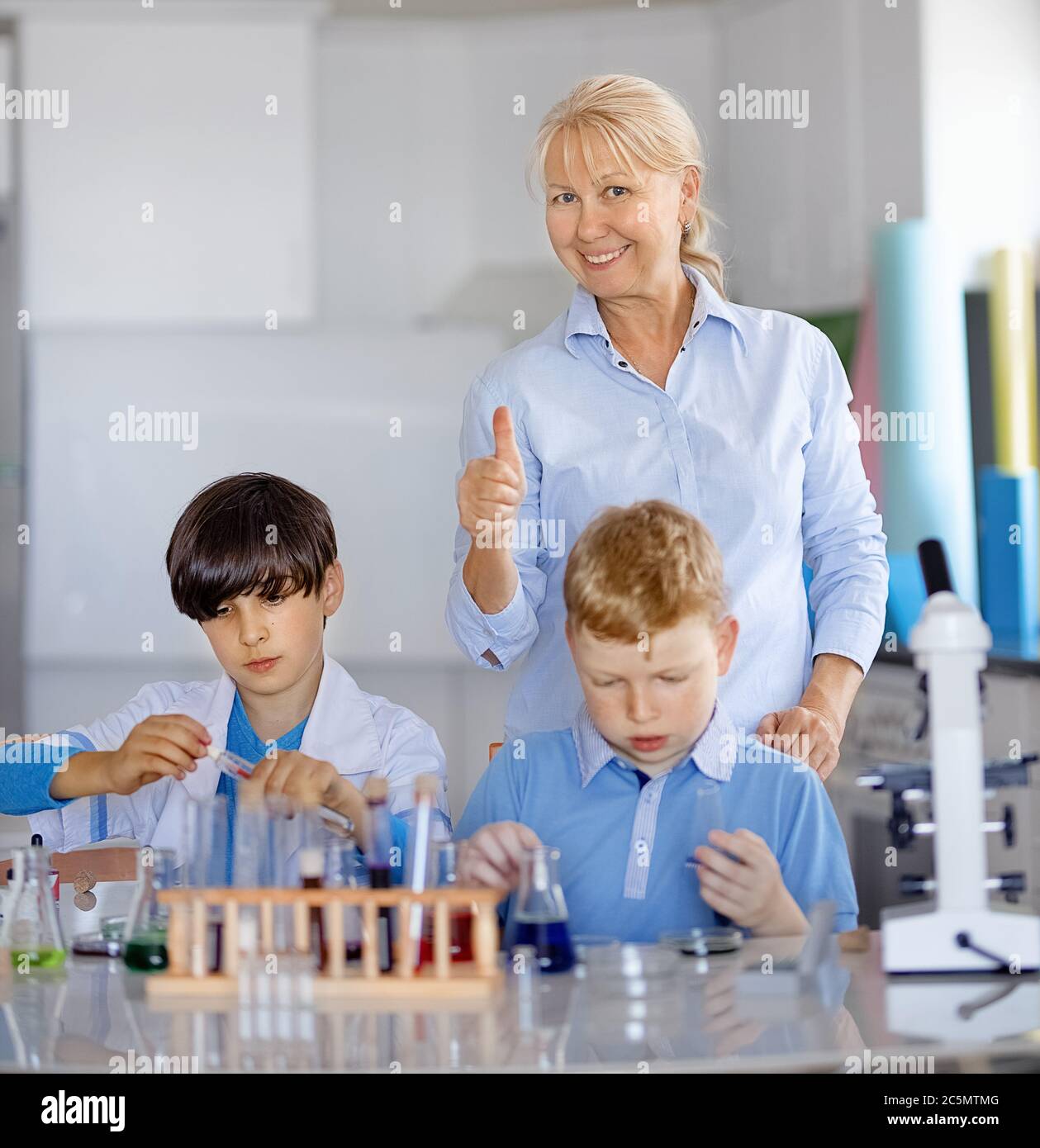 Lehrer und zwei Laborassistenten führen Experimente mit farbigen Flüssigkeiten durch Stockfoto