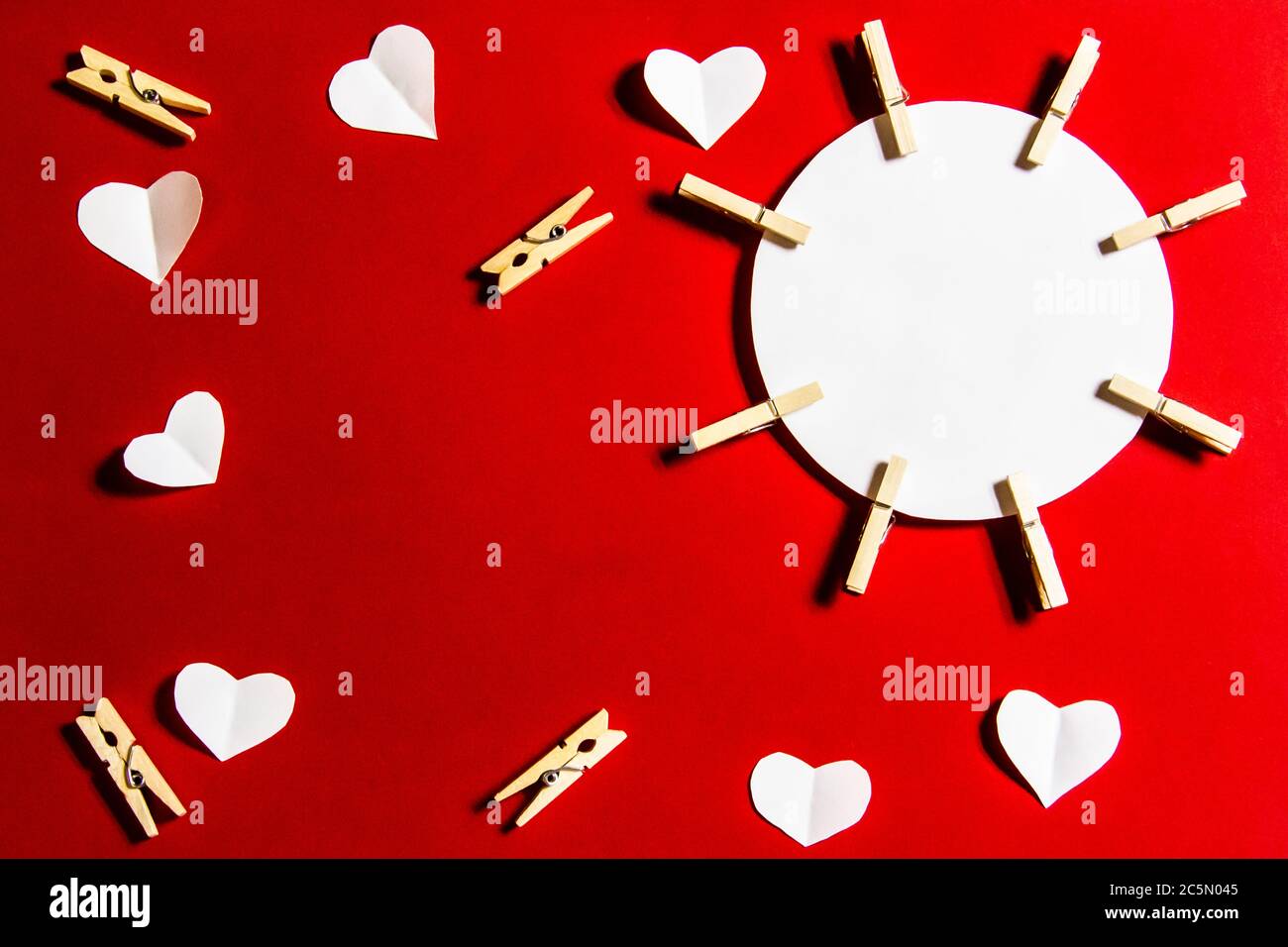 Komposition für Valentinstag. Wäscheklammern, Herzen und Papier für die Note vor einem roten Hintergrund. Elemente für Design oder Karte. Stockfoto