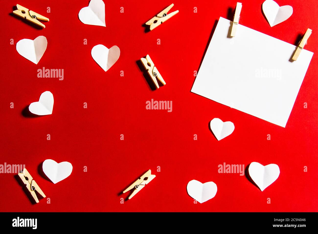 Komposition für Valentinstag. Wäscheklammern, Herzen und Papier für die Note vor einem roten Hintergrund. Elemente für Design oder Karte. Stockfoto