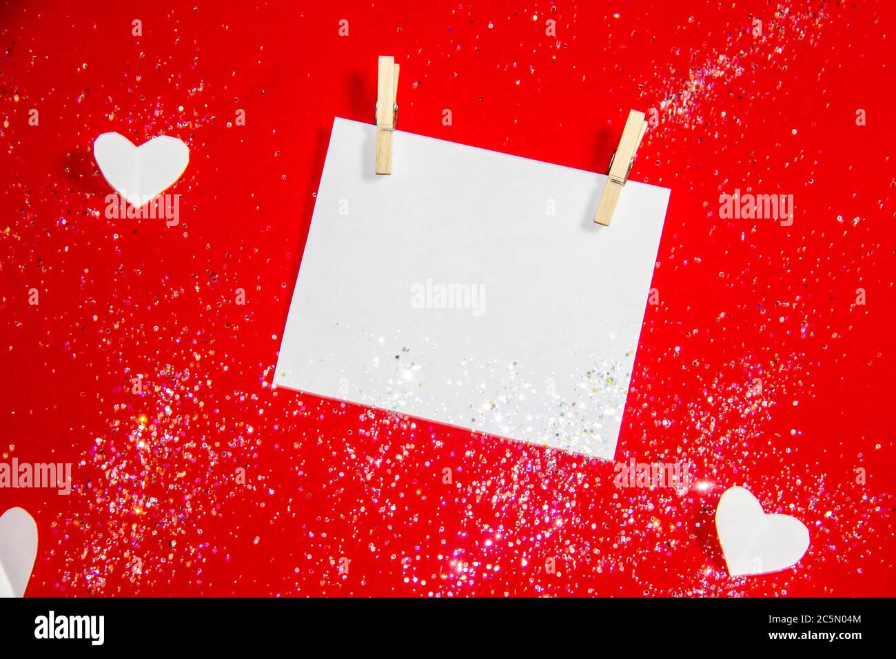 Komposition für Valentinstag. Wäscheklammern, Herzen und Papier für die Note vor einem roten Hintergrund. Elemente für Design oder Karte. Schöner roter Hintergrund Stockfoto