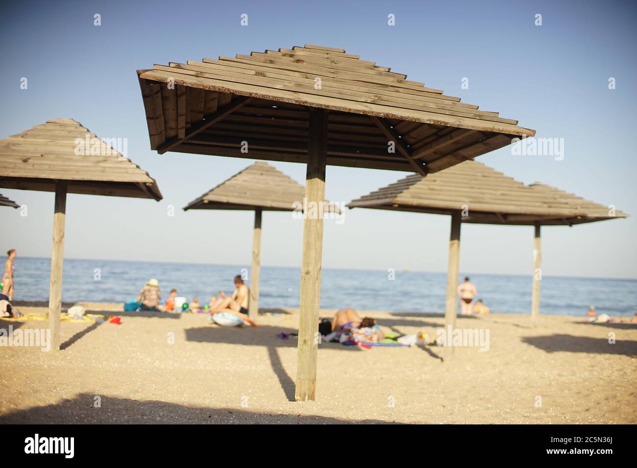 Hölzerne Strandüberdachen auf einem Meer Sandstrand. Auf einem unscharfen Hintergrund sonnen sich die Menschen Stockfoto