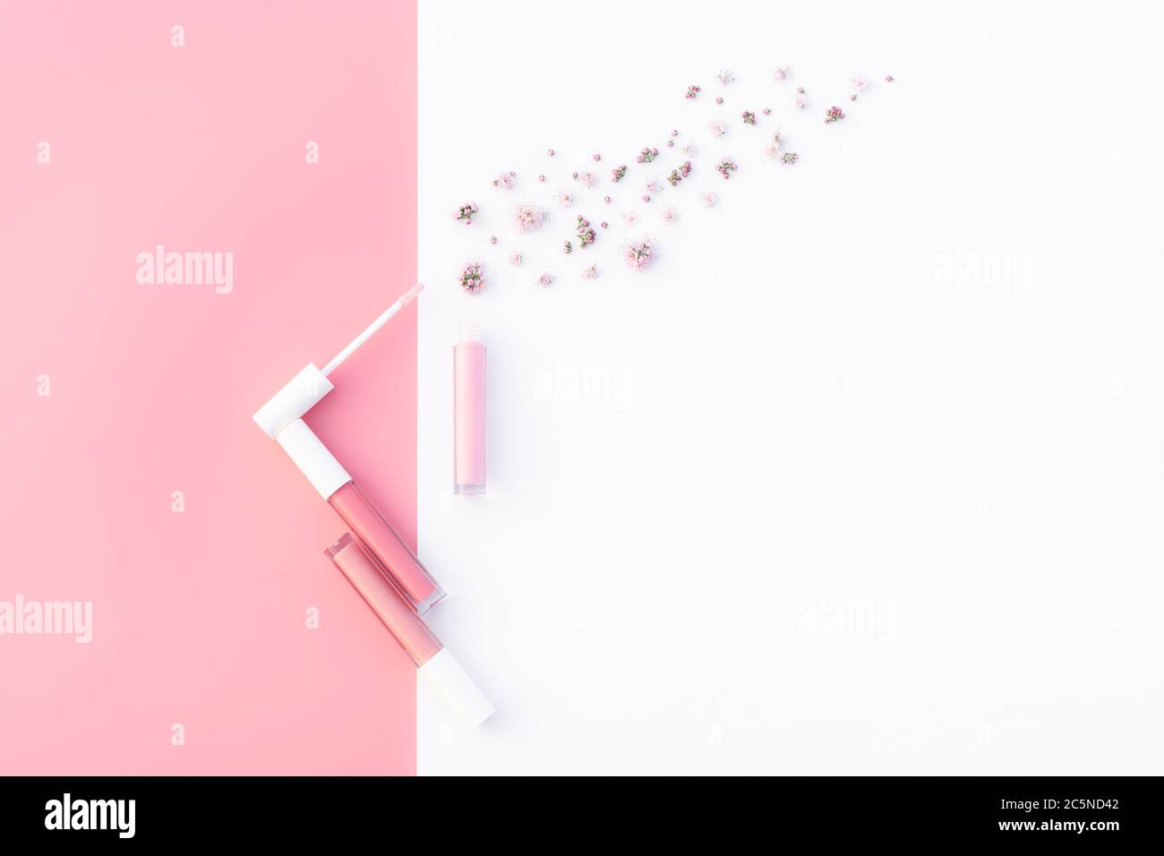 Trendige Design-Vorlage mit zartem rosa Lipgloss Layout geöffnet mit kleinen Blumen Dekoration auf pastellrosa und weißem Hintergrund. Flach liegend. Speicherplatz kopieren. Modell für Ihr Design. Stockfoto