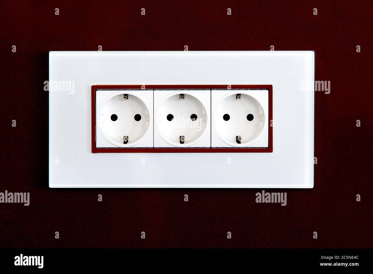 Steckdose mit Steckern für Standard-Stecker Typ F in weißem Kunststoffgehäuse an einer burgunderroten, glänzenden Steinwand. Stockfoto