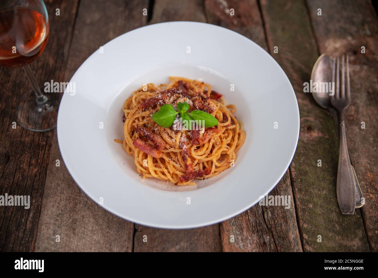 Pasta Carbonara. Spaghetti mit Speck, Parmesankäse und Basilikumblättern. Pasta Carbonara auf weißem Teller mit Parmesan auf dunklem Hintergrund. Italienisches Speisekonzept. Stockfoto