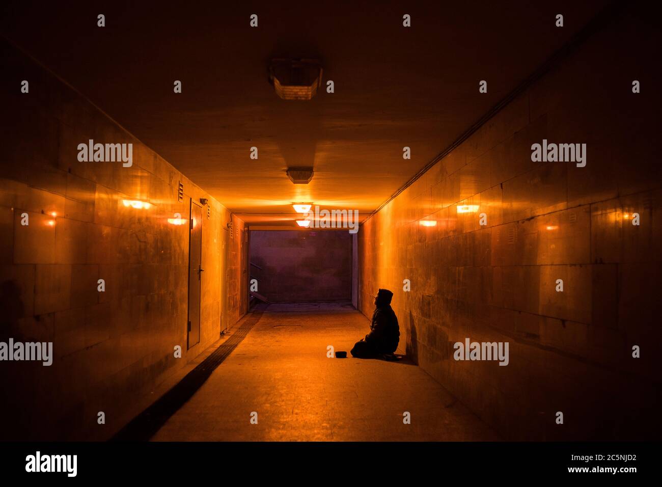 Obdachloser Bettler auf den Knien bittet in einer dunklen Unterführung um Almosen. Stockfoto
