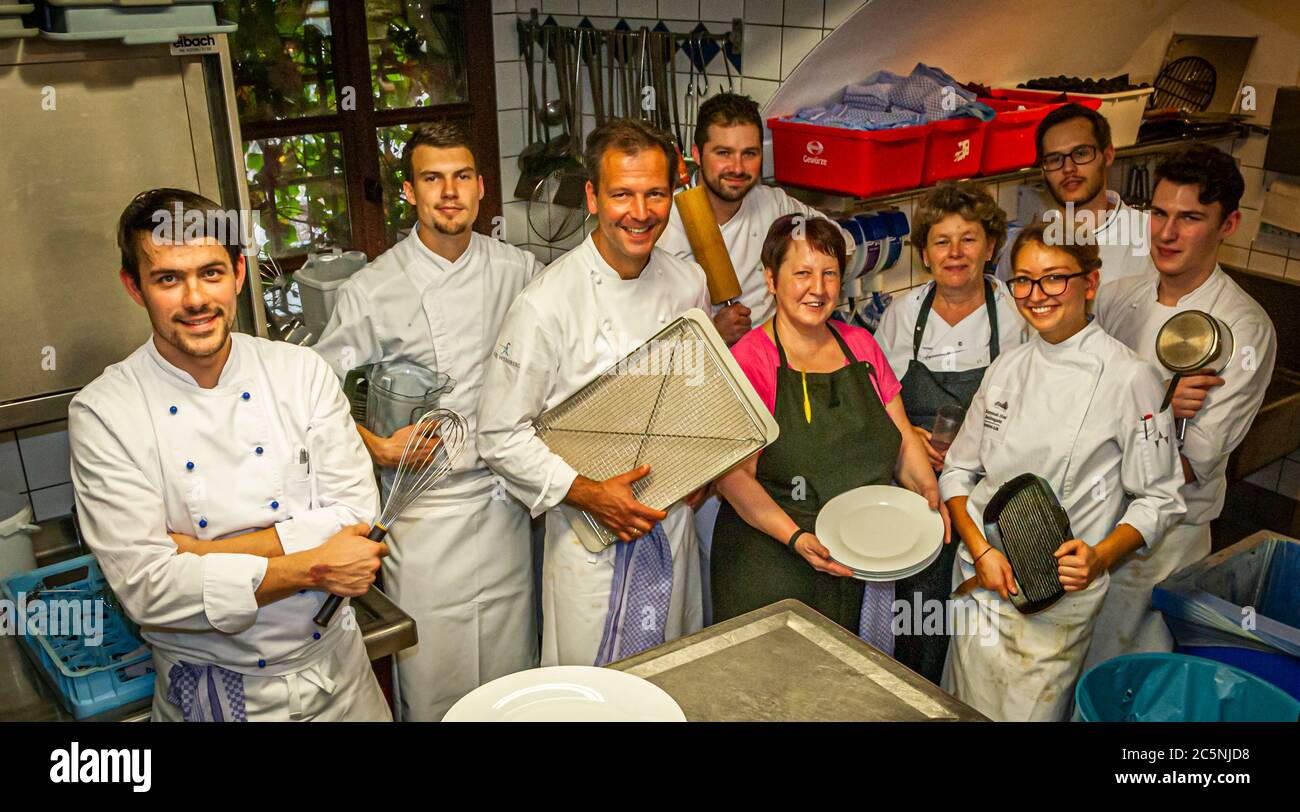 In der engen Spülküche des Schlosses Wernberg, Wernberg-Köblitz, Oberpfalz, Deutschland, kommen alle vorbei – deshalb wird hier auch das Gruppenfoto des Küchenteams um den Michelin-Sterne-Koch Thomas Kellermann gemacht. Er hält scherzhaft ein Kühlregal hoch, während seine Mitarbeiter mit einem Schneebesen, Tellern und Küchenutensilien posieren. Stockfoto