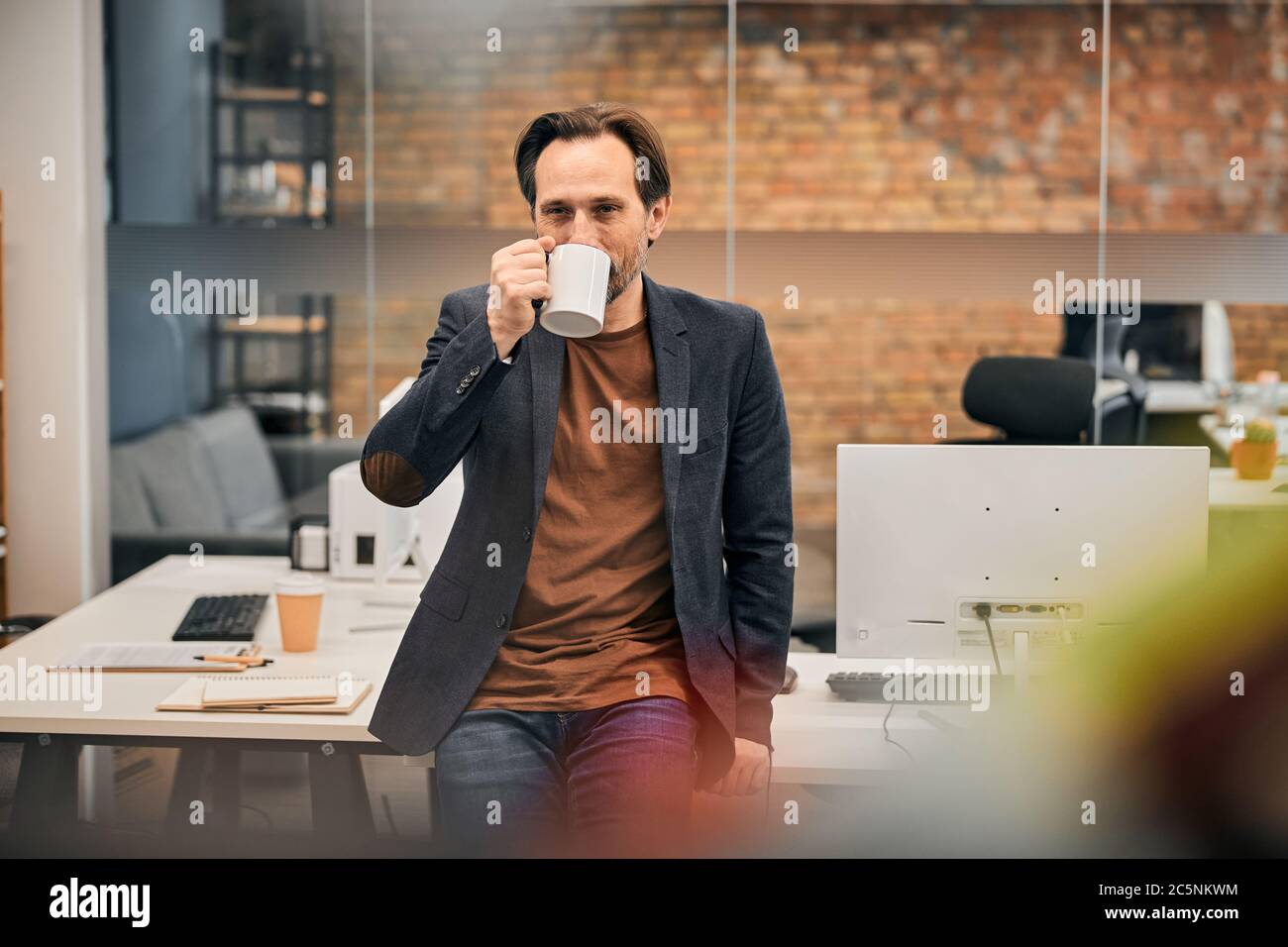 Bärtiger Mann in braunem Hemd und schwarzer Jacke, der bei der Arbeit ruht Stockfoto
