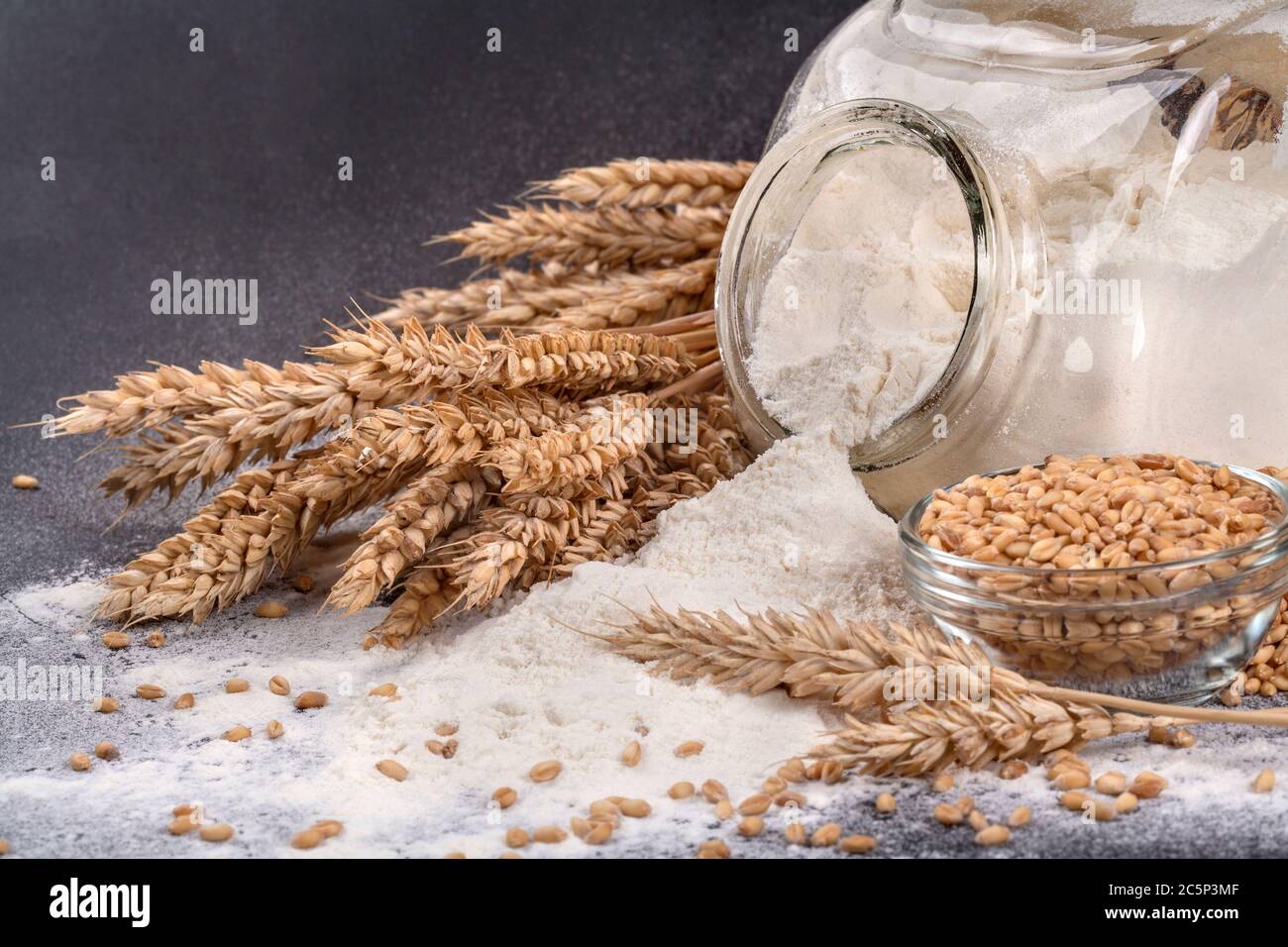 Mehl und Getreide auf schwarzem Hintergrund zusammen mit bestreut Ein Glas Stockfoto