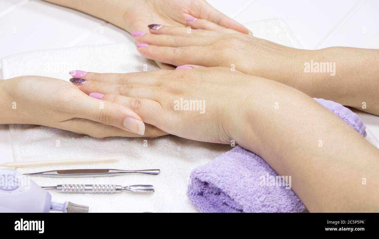 Der Manikurist hält die Hände des Kunden. Eine Frau zeigt ihre Hände mit bemalten Nägeln. Rosa, Nacktremaniküre, Nailart, Glitzer-Polnisch. Handpflege im Spa. Bea Stockfoto