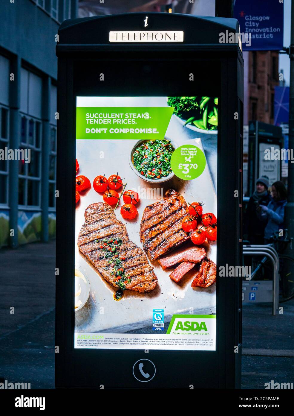 Asda-Werbung für Steaks und frisches Fleisch am Telefonkiosk, beleuchtet in der Nacht, Glasgow, Schottland, Großbritannien Stockfoto
