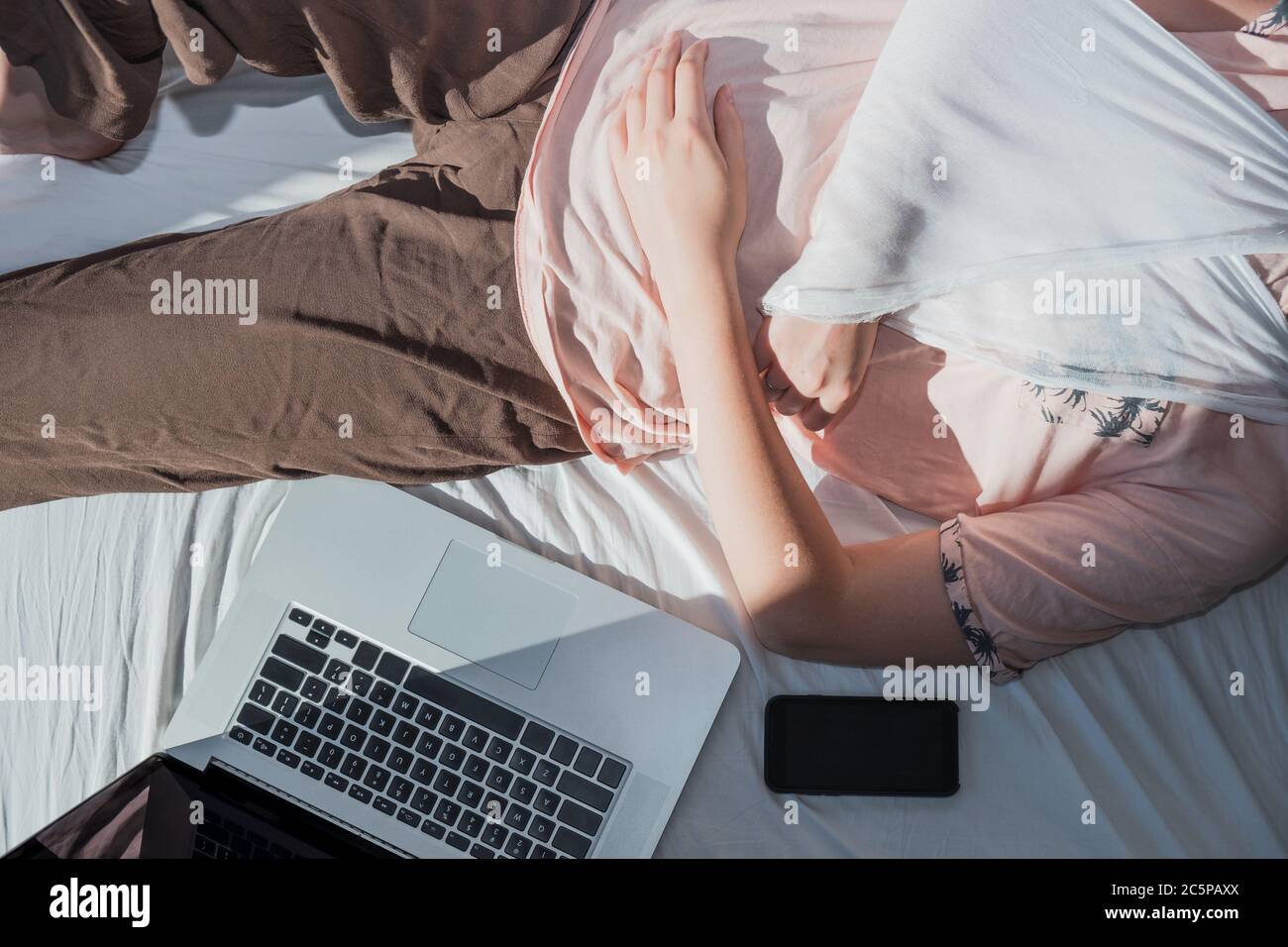 Frau mit verwundeten Arm liegt im Bett neben einem Computer und Telefon. Konzept der Remote-Arbeit, nicht in der Lage, produktiv zu sein, im Krankenstand zu bleiben Stockfoto