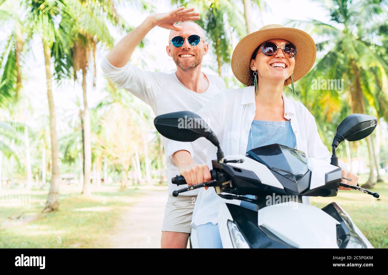 Glücklich lächelnd Paar Reisende Reiten Motorrad Roller unter Palmen. Thailand tropischen Urlaub Konzept Bild Stockfoto