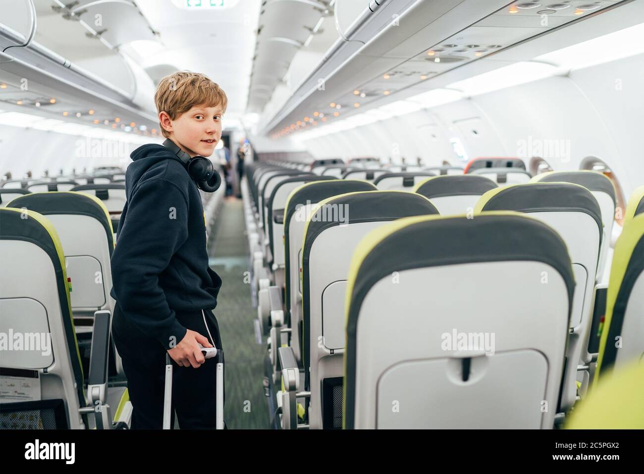 Lächelndes blondes Haar Teenager-Porträt Aufenthalt in Flugkorridor mit Kopfhörer mit Kabine Trolley Tasche. Kinder reisen oder unbegleitetes Kind in ai Stockfoto