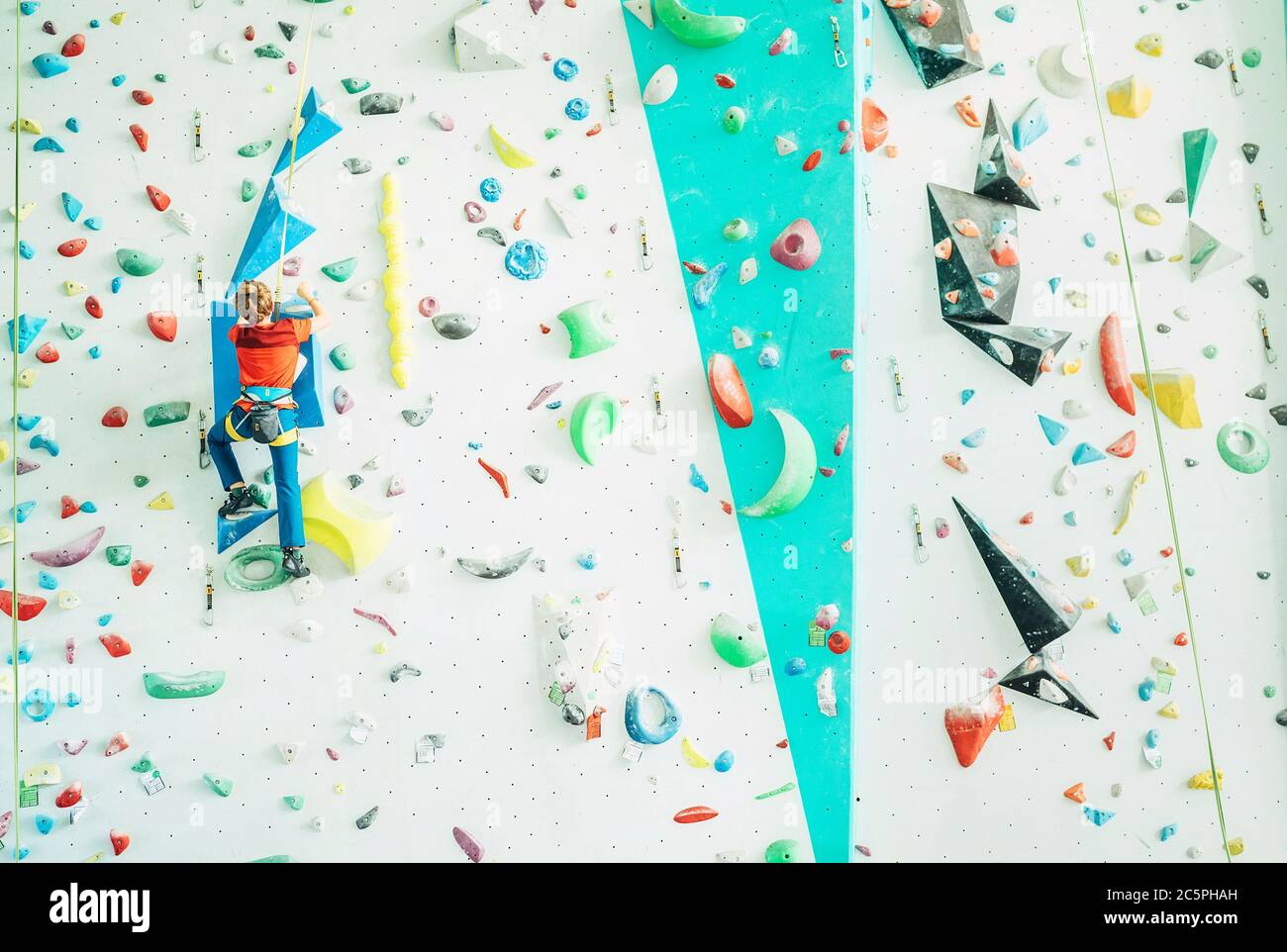 Teenager Junge in Indoor Kletterwand Halle. Boy klettert mit einem Auto-Sicherungssystem und Klettergurt. Aktive Teenager Zeit verbringen Konzept imag Stockfoto