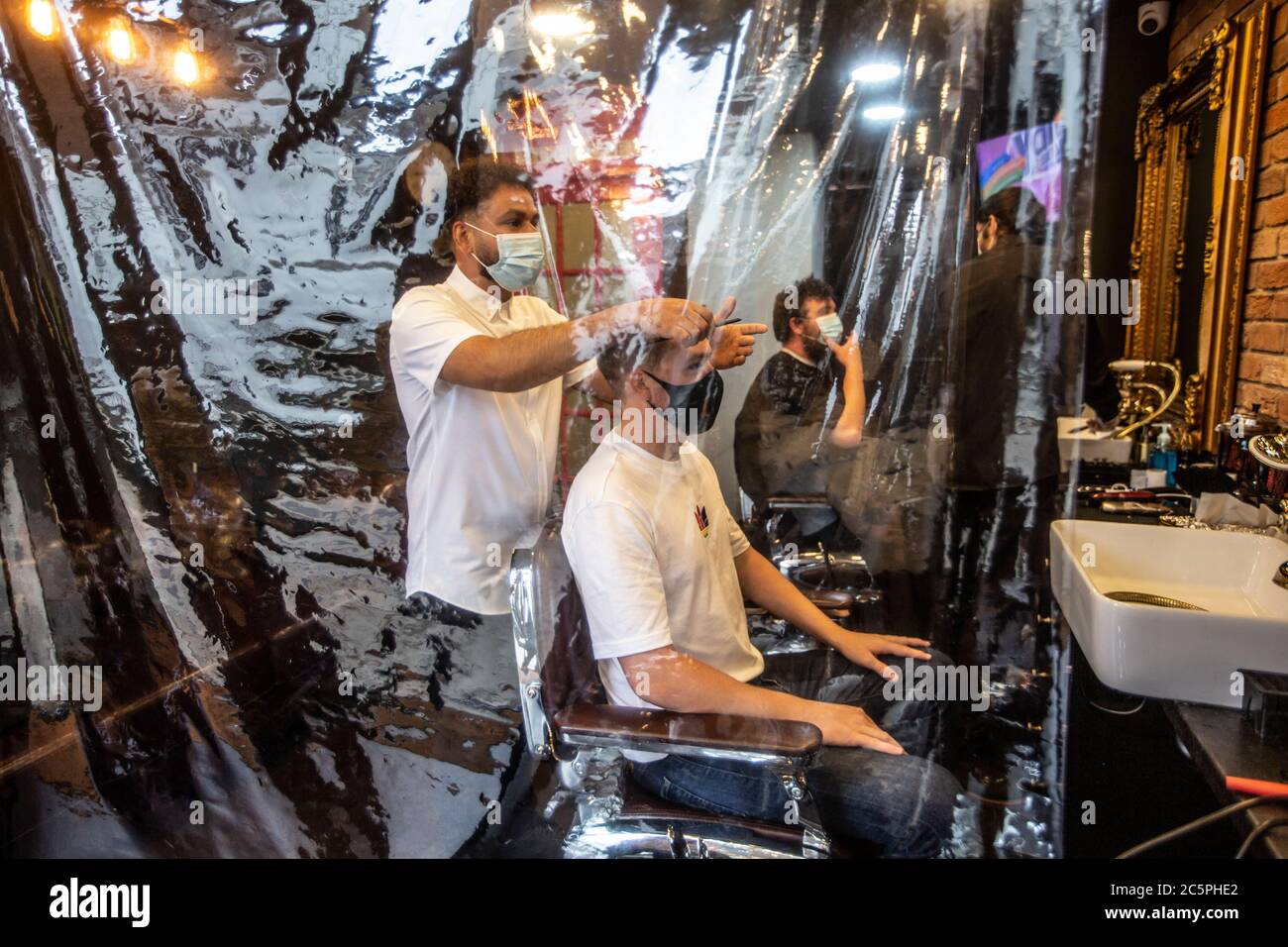 Gentleman's Barber Friseursalon wurde nach der Sperre durch Coronaviren mit vorsorglichen Plastikfolien und Stylisten mit Gesichtsmasken wiedereröffnet. Stockfoto