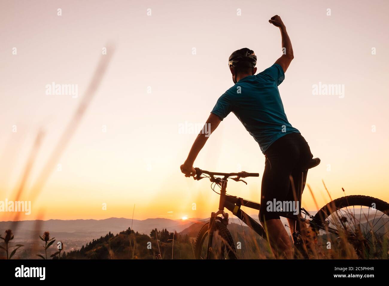 Mann Biker Mann trifft einen Sonnenuntergang auf dem Hügel. Er einen Arm aufsteigende Gruß an einem anderen erfolgreichen Tag zu Ende. Active Sport People Konzept Bild Stockfoto