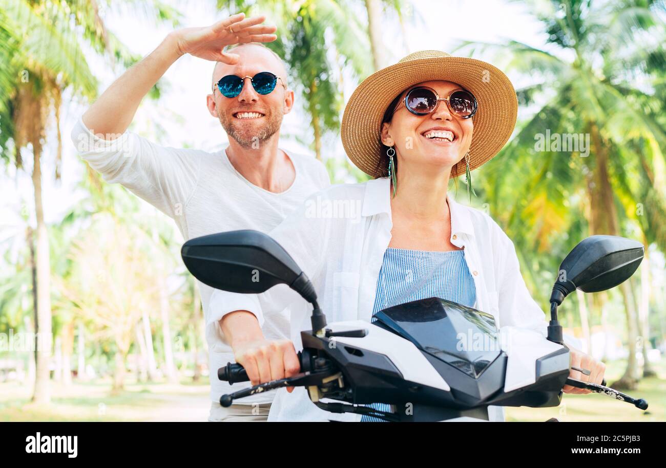 Glücklich lächelnd Paar Reisende Reiten Motorrad Roller unter Palmen. Thailand tropischen Urlaub Konzept Bild Stockfoto