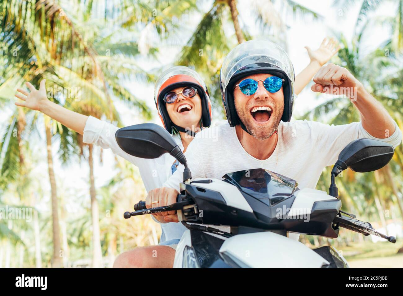 Glücklich lächelndes Paar Reisende Reiten Motorrad Roller in Sicherheitshelmen während tropischen Urlaub unter Palmen auf Ko Samui Insel in Thailand Stockfoto