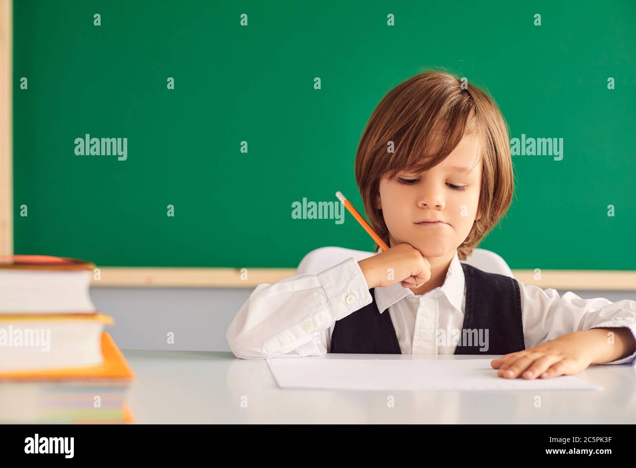 Zurück zur Schule. Ernsthafter kleiner Junge, der etwas im Notebook am Schreibtisch im Klassenzimmer schreibt, Platz zum Kopieren. Fleißtes Kind, das in der Schule studiert Stockfoto