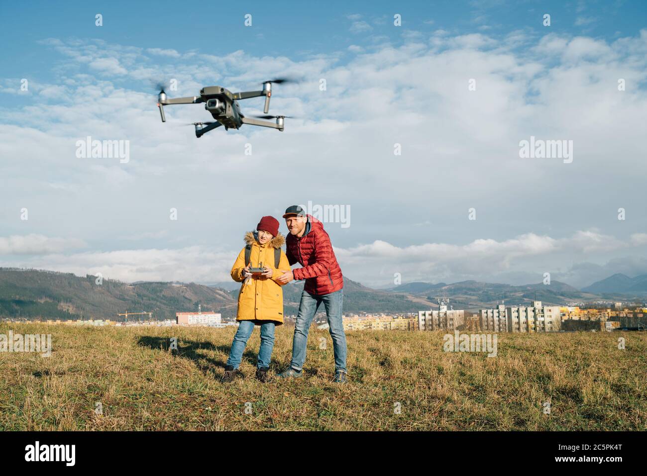 Teenager Junge Sohn gekleidet gelbe Jacke und Vater pilotieren eine moderne digitale Drohne mit Fernbedienung. Moderne Technologie entwickelt Konzept Bild Stockfoto