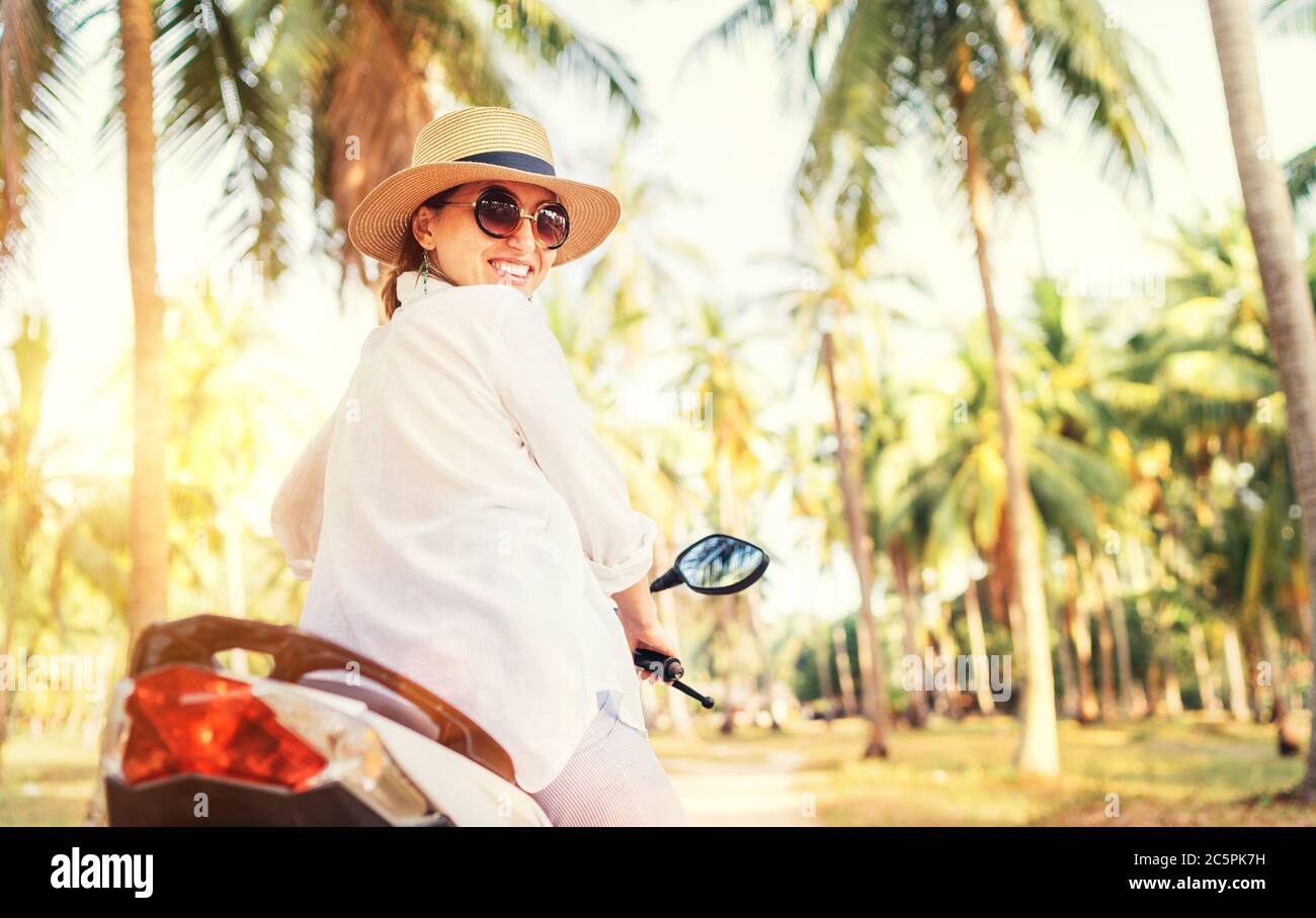 Glücklich lächelnde Frau in Strohhut und Sonnenbrille Reiten Motorrad unter Palmen die Bäume. Sorglos warm Counries Urlaub Zeit Konzept Bild. Stockfoto