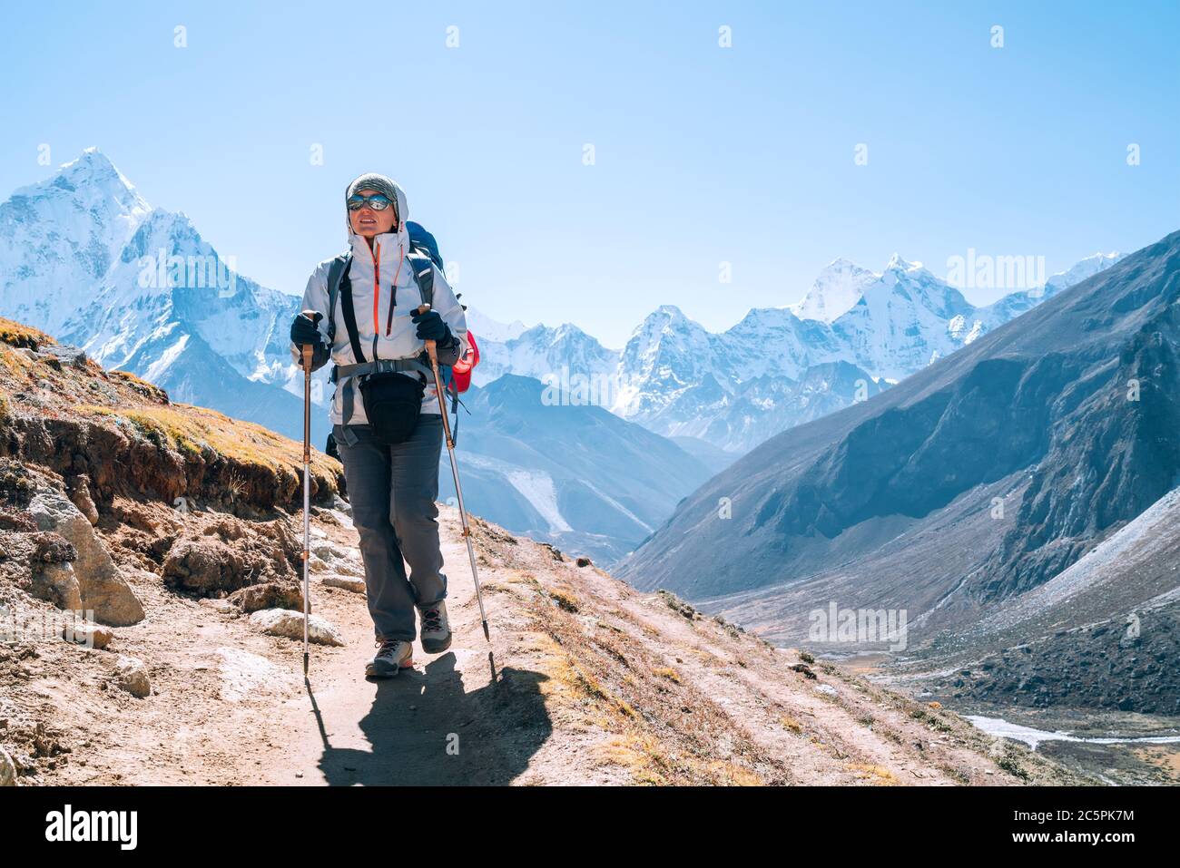 Junge Wandererin Backpacker-Frau, die während der Route des Everest Base Camps in der Nähe von Dingboche, Nepal, mit Wanderstöcken unterwegs ist. AMA Dablam 6812 m. Stockfoto