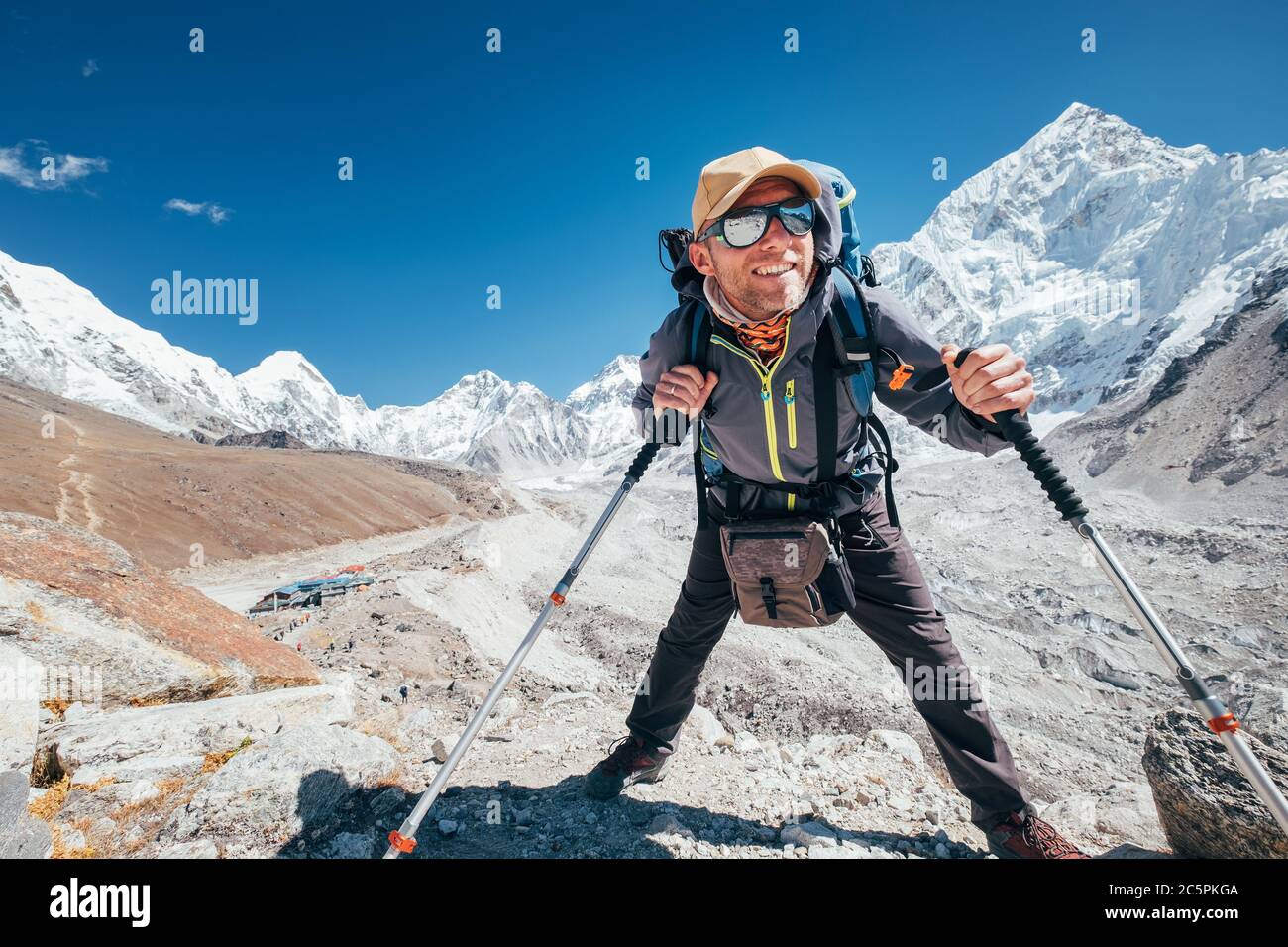 Portrait eines lächelnden Wanderers mit Nuptse 7861 m Gipfel und Gorak shep Siedlungshintergrund mit Trekkingstöcken, UV-schützende Sonnenbrille. Er genießt es Stockfoto