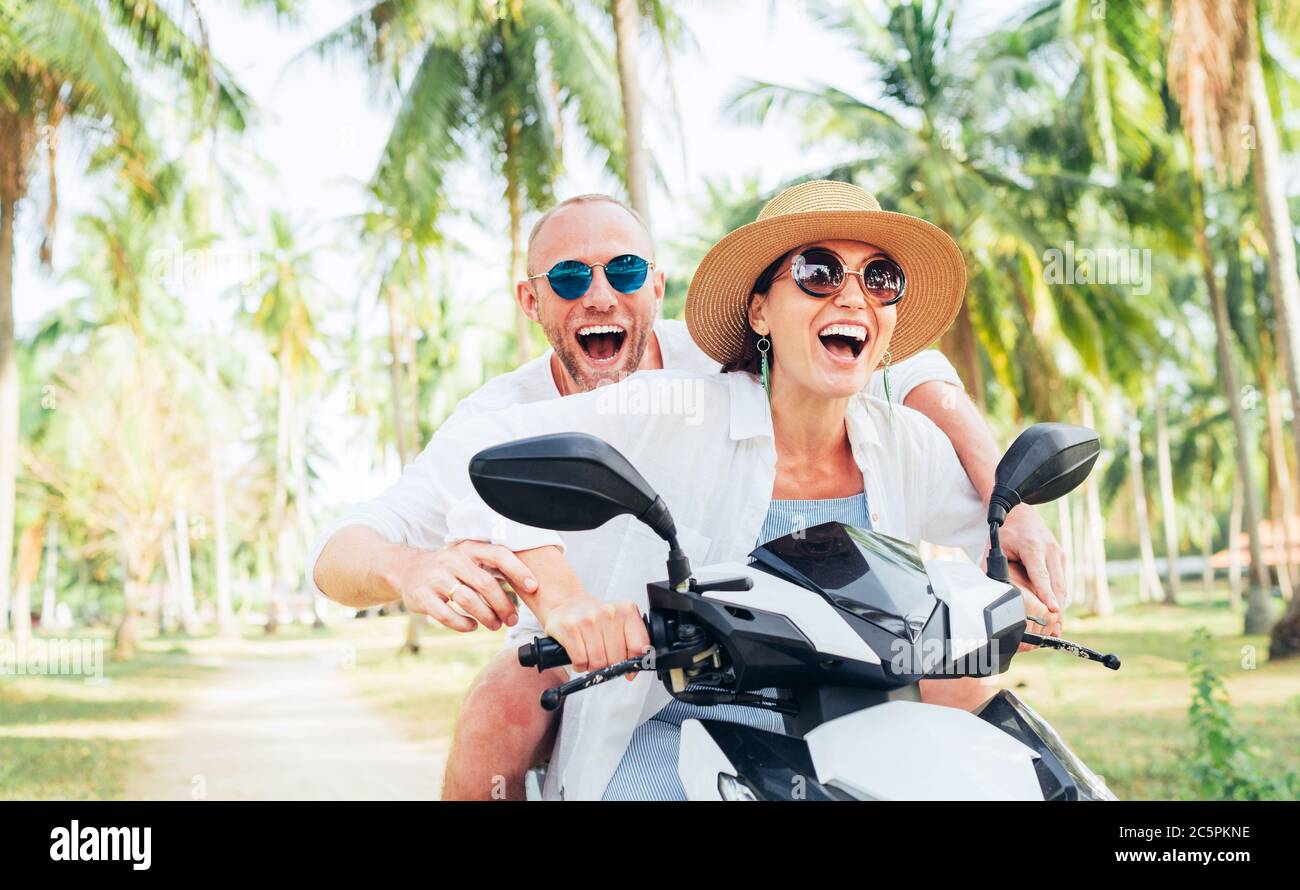 Lächelnd verliebt reiten die beiden Reisenden auf dem Motorrad unter Palmen in ihrem Inselurlaub Stockfoto