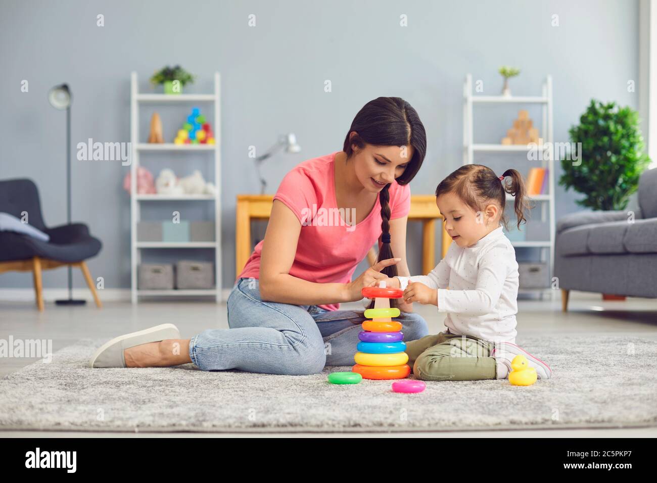 Hispanische Mutter und Tochter spielen mit Spielzeug, während sie auf dem Boden im Zimmer sitzen. Stockfoto