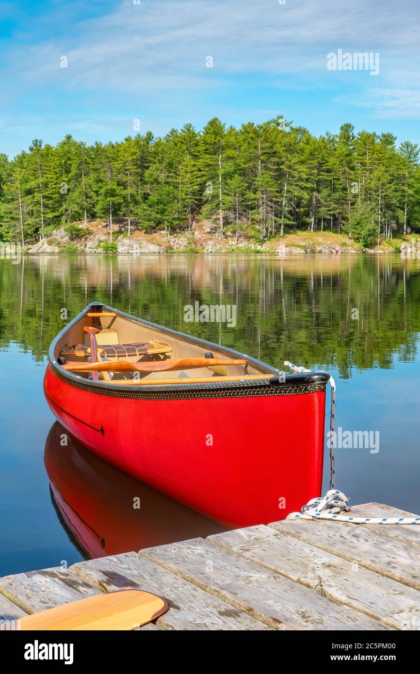 Rotes Kanu an einem Dock auf dem ruhigen Wasser von Stony Lake gebunden, wenn es ruhig und gelassen ist. Stockfoto