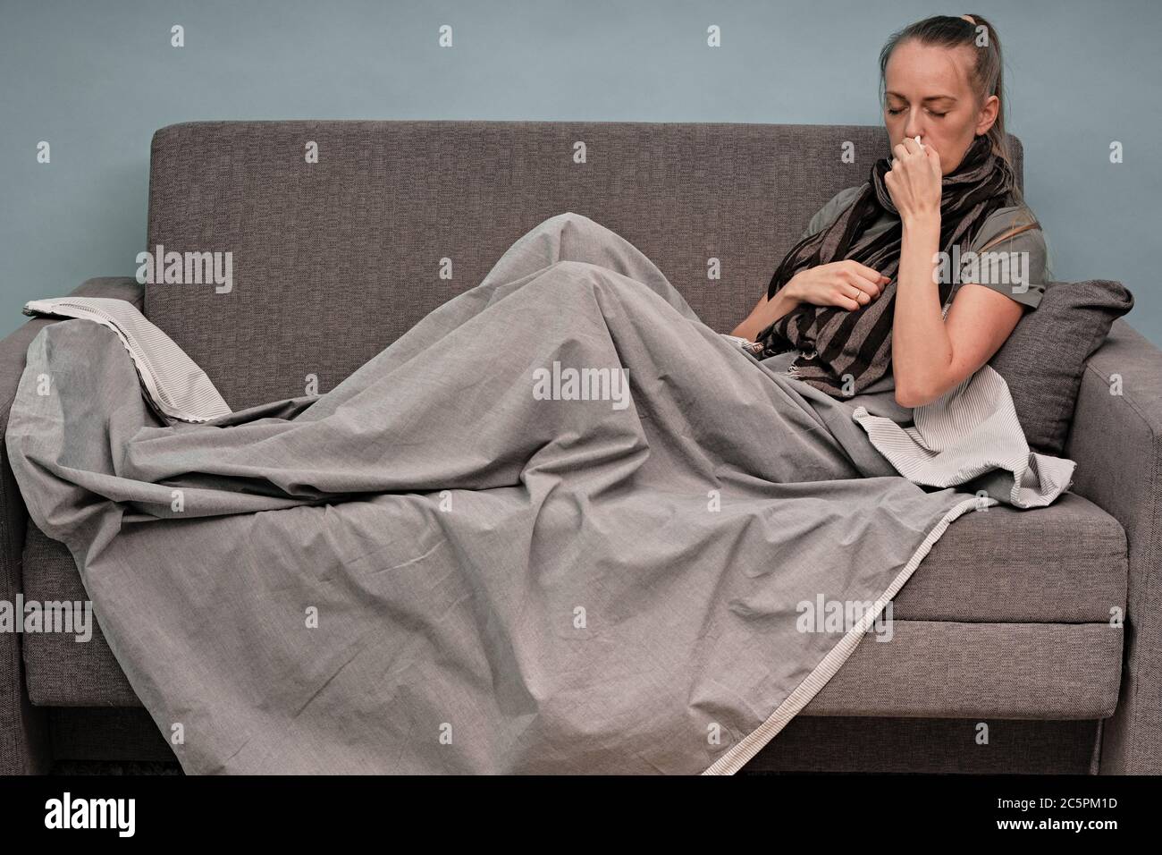 Das Mädchen ist zu Hause krank. Auf einer Couch sitzend, in eine Decke gewickelt, ein Schal um seinen Hals. Coronavirus. Stockfoto