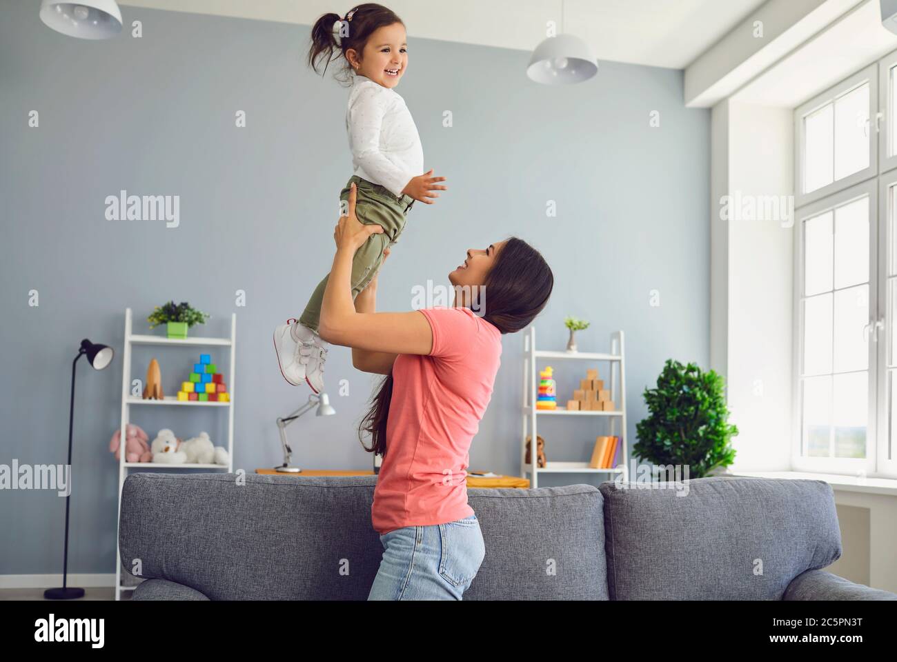 Liebevolle Mutter mit ihrer kleinen Tochter Spaß zu Hause. Eltern spielen Spiel mit ihrem Kind, werfen sie in die Luft Stockfoto