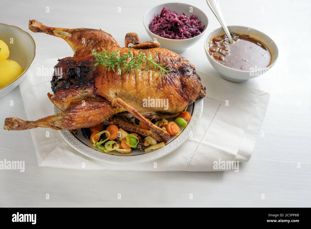Geröstete Ente mit Apfel, Pflaumenfüllung, serviert mit Gemüse, Rotkohl, Kartoffeln und Sauce, festliches Weihnachtsessen auf einem weißen Tisch, Kopierraum, s Stockfoto