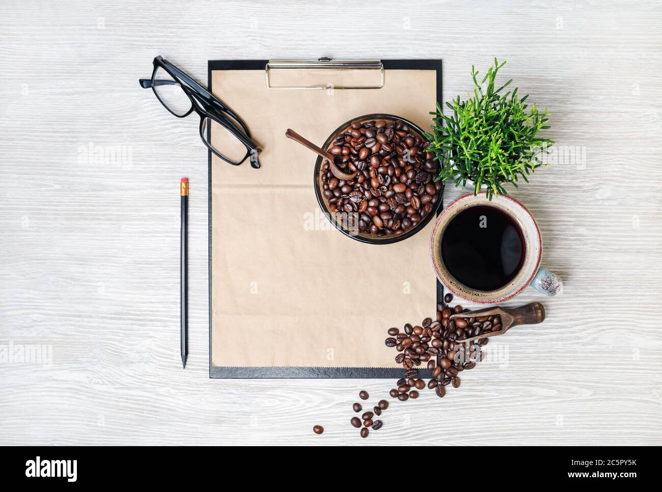 Schreibwaren und Kaffee. Klemmbrett mit Kraftpapier, Kaffeetasse, Kaffeebohnen, Bleistift, Gläser und Pflanze auf hellem Holzhintergrund. Flach l Stockfoto