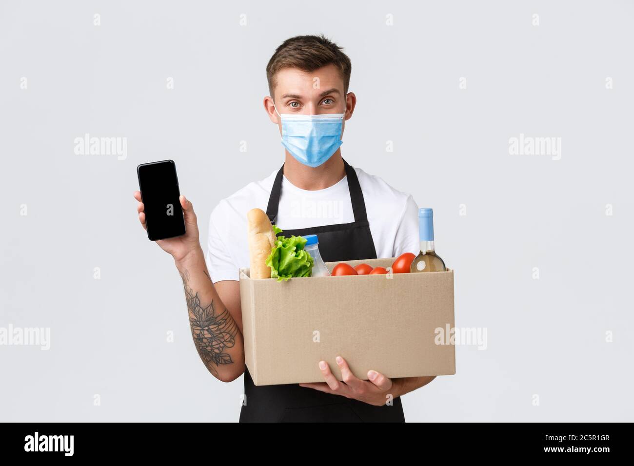 Covid-19, kontaktloses Shopping- und Lebensmittelzulieferkonzept. Schöner Verkäufer in medizinischen Maske schlagen Weg der Bestellung Lebensmittel mit Stockfoto