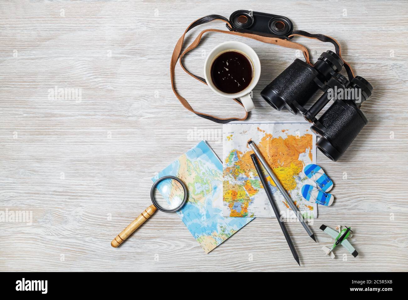 Reiseplan Hintergrund. Karte, Fernglas, Lupe, Stifte, Kaffeetasse, Flugzeug und Flip Flops auf hellem Holzhintergrund. Draufsicht. Flach liegend. Stockfoto