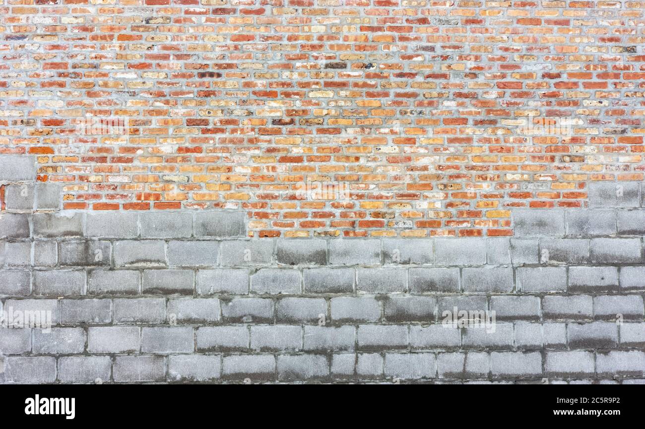 Kombination aus grauem Schlackenkerblock und traditioneller roter und oranger Ziegelwand. Stockfoto