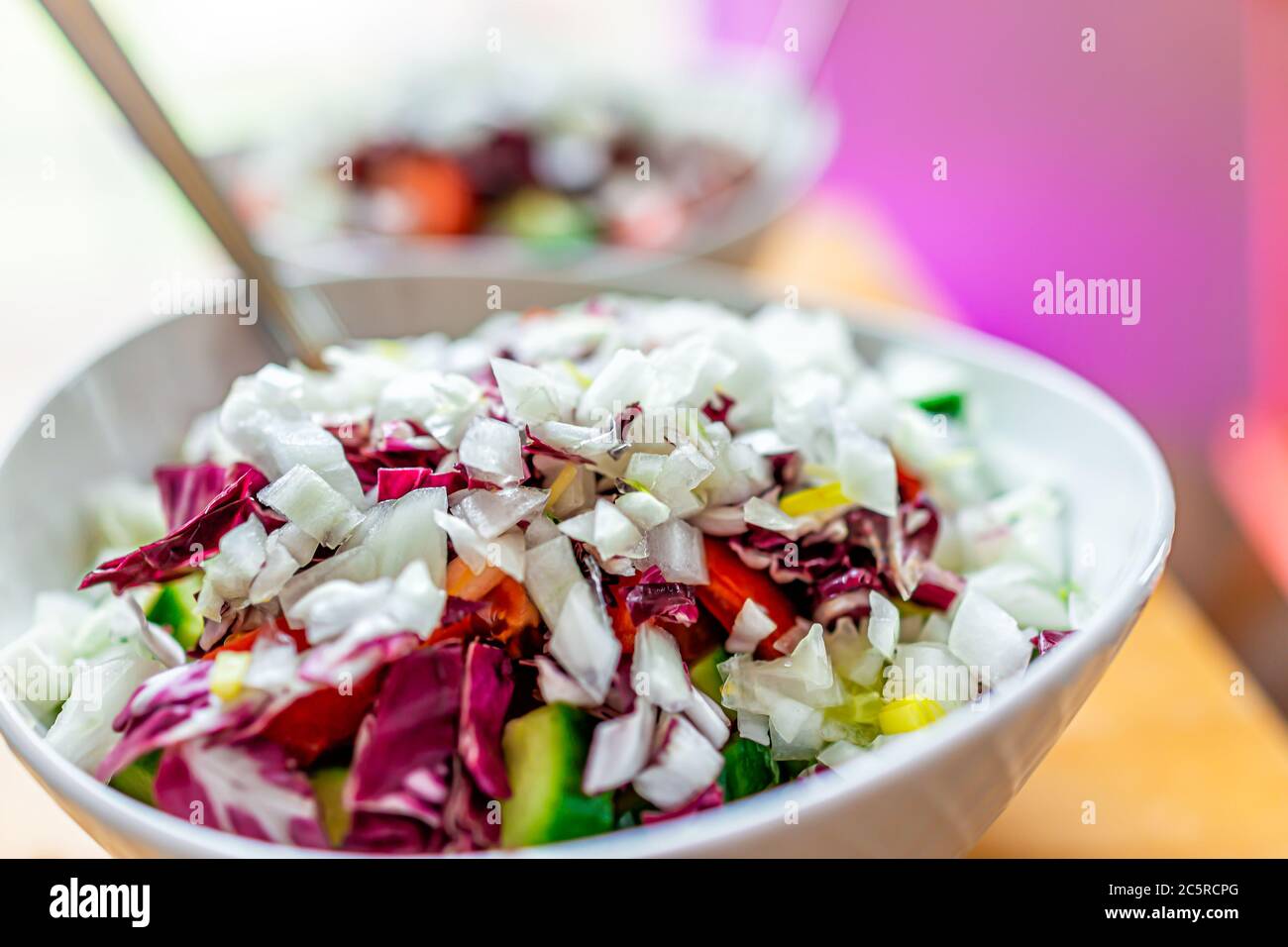 Vegane Salatschüssel mit Radicchio und gehackten Zwiebeln, Gurken und Endive Salat Zichorien lila Blätter für Mittag-oder Abendessen und rosa Hintergrund Stockfoto