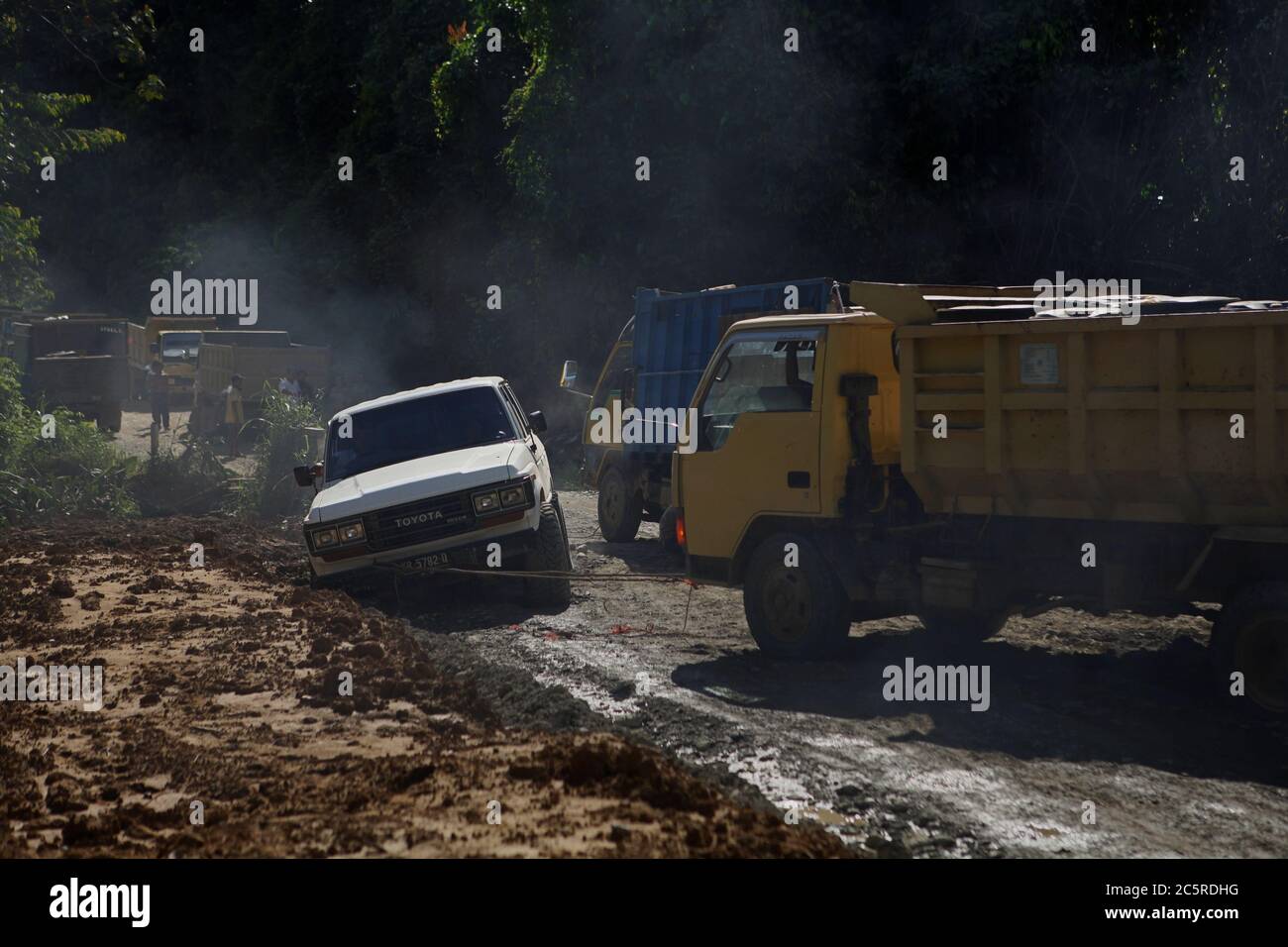 Ein LKW zieht ein Auto, das im Schlamm stecken blieb, da eine neue Straßeninfrastruktur in einem abgelegenen Gebiet innerhalb der Kapuas Hulu Regentschaft, West Kalimantan Provinz, Indonesien entwickelt wird. Archivfoto (2012). Im abgelegenen Kalimantan verlassen sich lokale Gemeinden seit Jahrzehnten auf Flüsse und Wanderwegen für Mobilität und Transport. Die neue Straße wird die Städte Melak (Ost-Kalimantan Provinz) und Putussibau (West-Kalimantan Provinz) auf ihrer längsten Spannweite verbinden und wird voraussichtlich mindestens die Hälfte der traditionellen Reisezeit zwischen allen verbundenen Städten und Dörfern reduzieren. Stockfoto