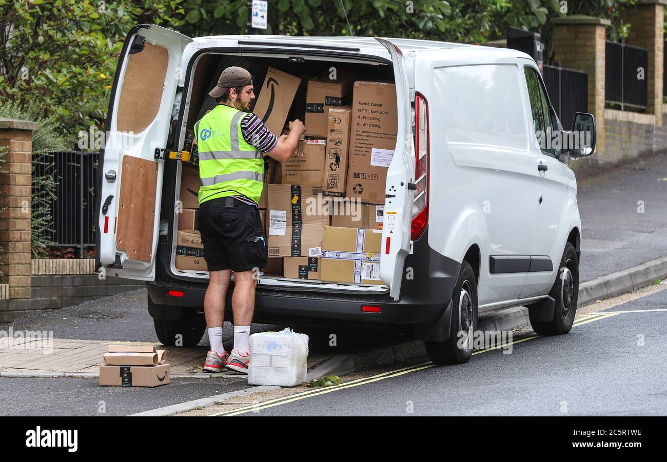 Ein Lieferfahrer, der einen kompletten weißen Van mit Paketen inklusive mehreren für Amazon bereit zur Lieferung verpackt, während er auf einer doppelten gelben Linie geparkt ist Stockfoto
