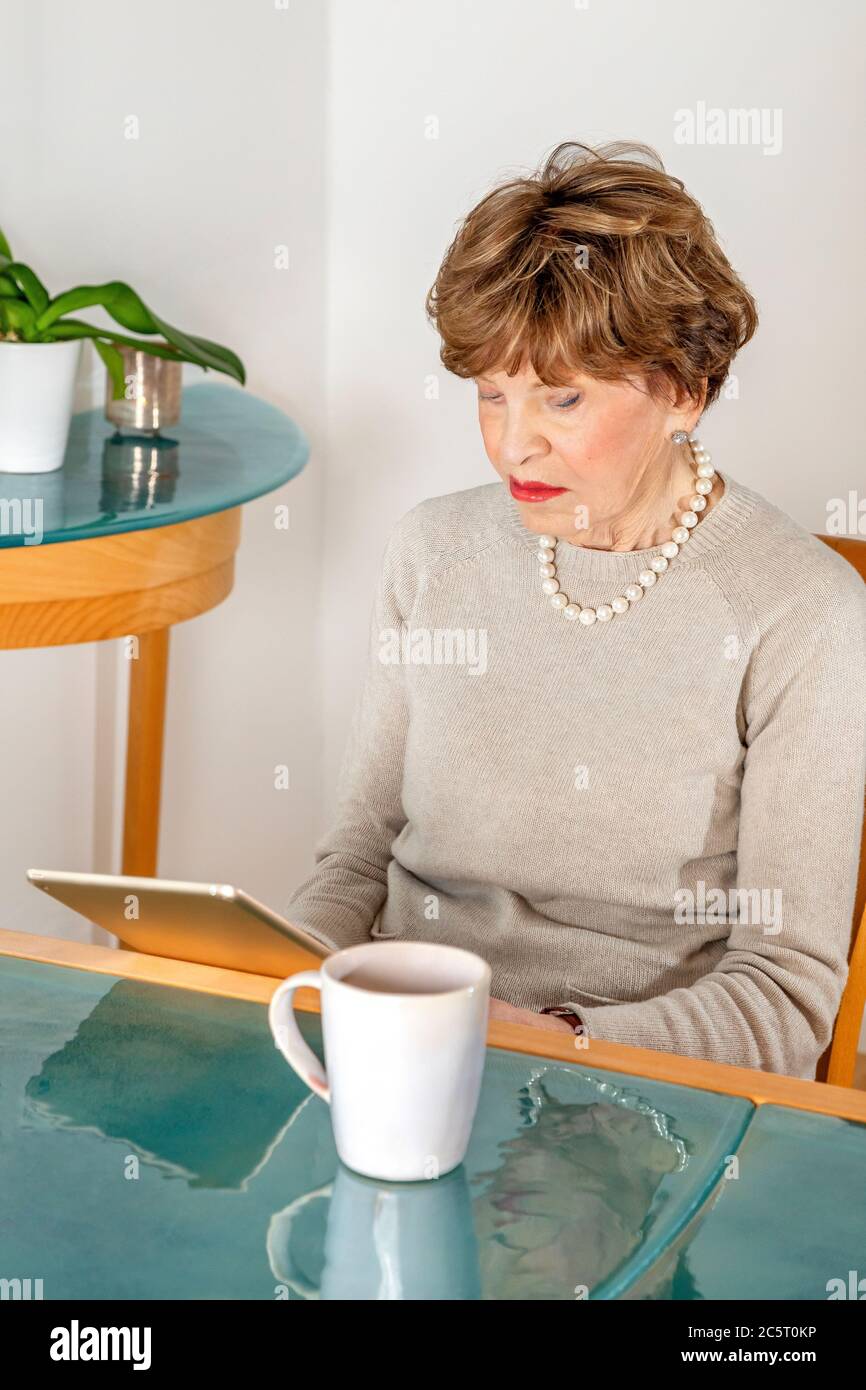 Achtzig Jahre alte sitzende Frau liest ihr ipad Stockfoto