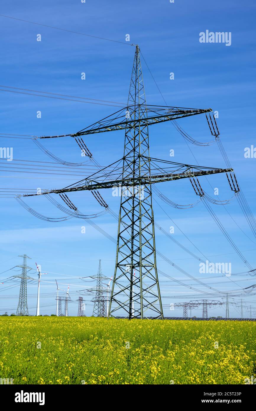 Ein Strommasten, Stromleitungen und einige Windturbinen in Deutschland gesehen Stockfoto