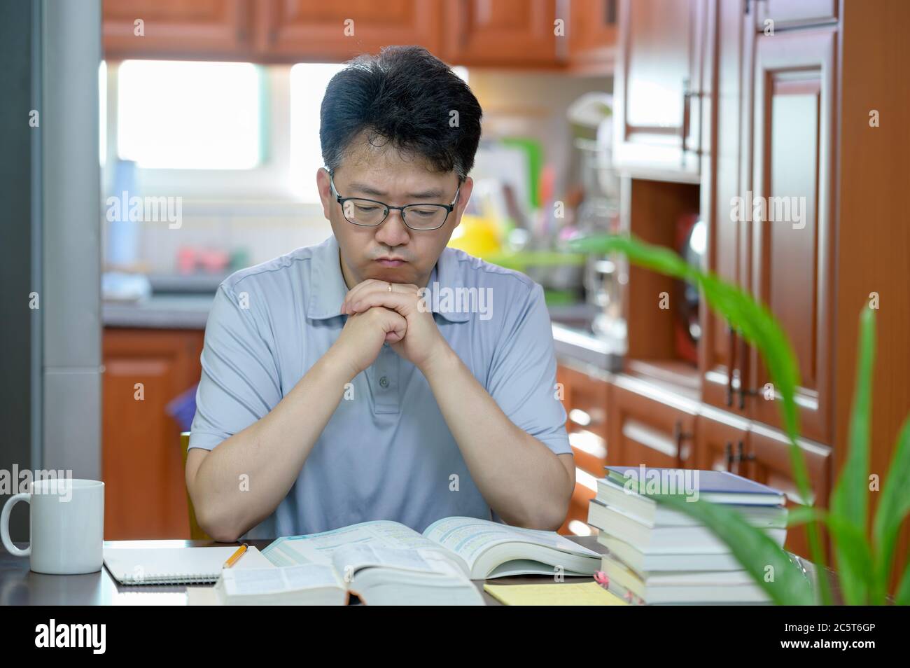 Asiatischer Mann mittleren Alters, der zu Hause am Schreibtisch sitzt, ein Buch liest und studiert. Stockfoto