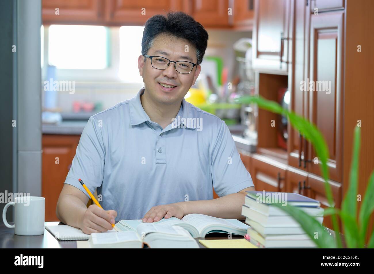 Asiatischer Mann mittleren Alters, der zu Hause am Schreibtisch sitzt, ein Buch liest und studiert. Stockfoto