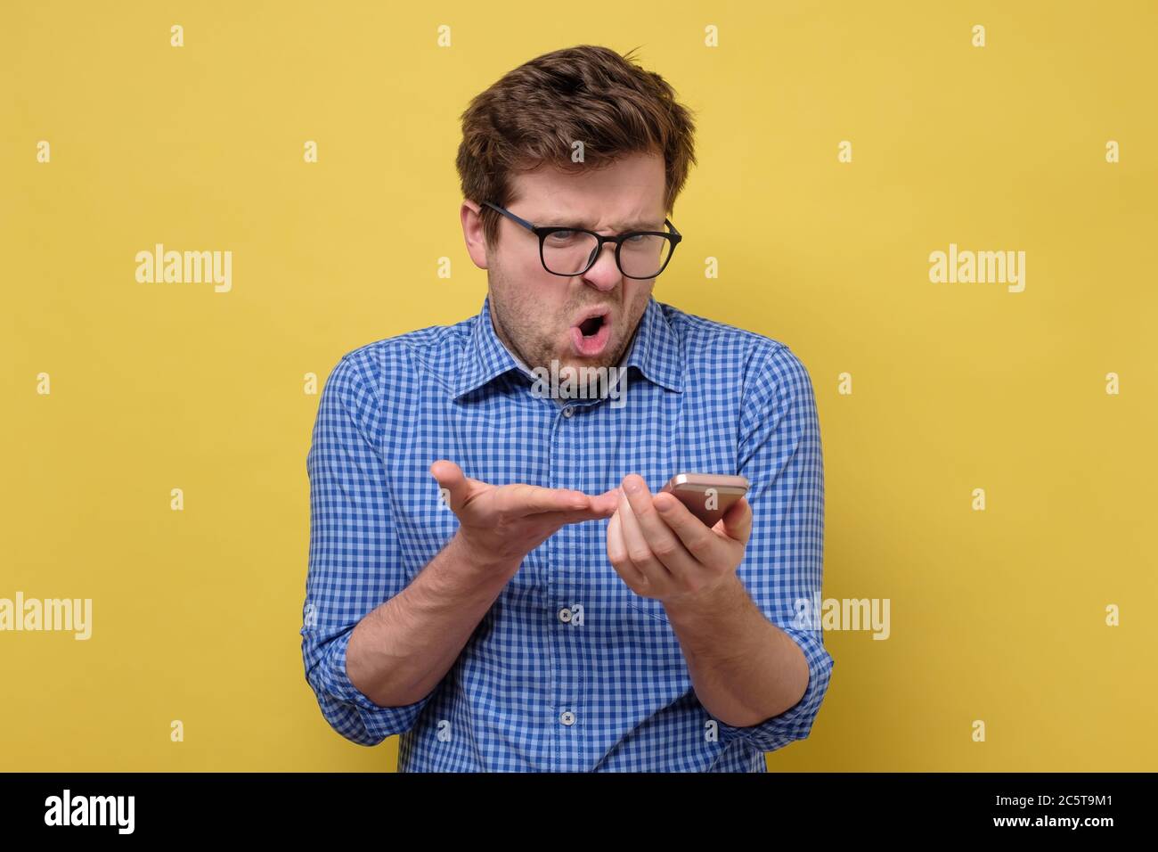 Wütender Mann mit einem Telefon in den Händen, der SMS liest Stockfoto