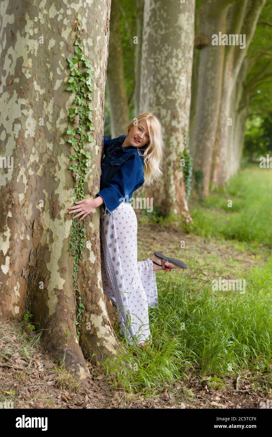 Schöne junge blonde Frau umarmt einen riesigen alten Baum Stockfoto