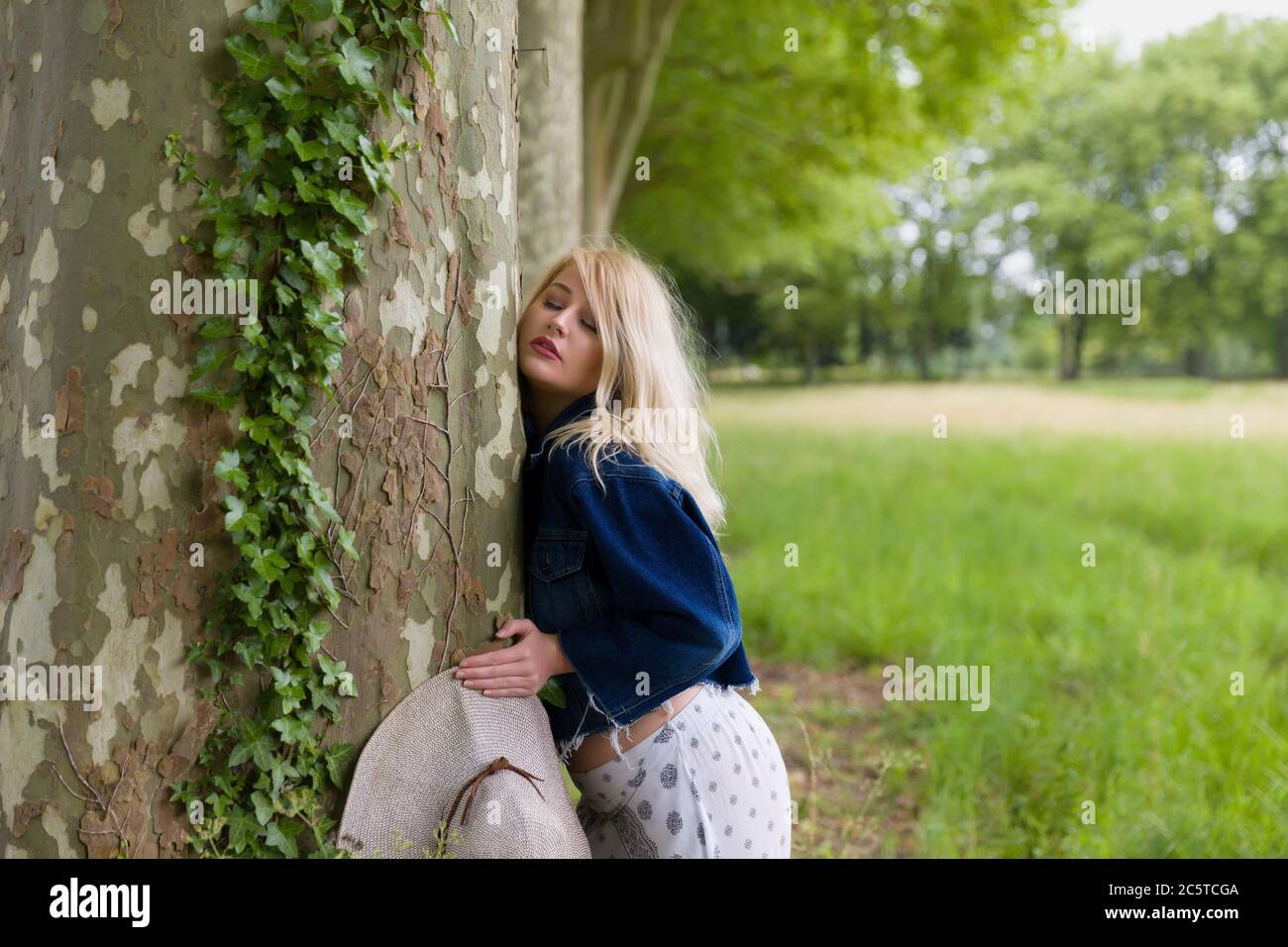 Schöne junge blonde Frau umarmt einen riesigen alten Baum Stockfoto