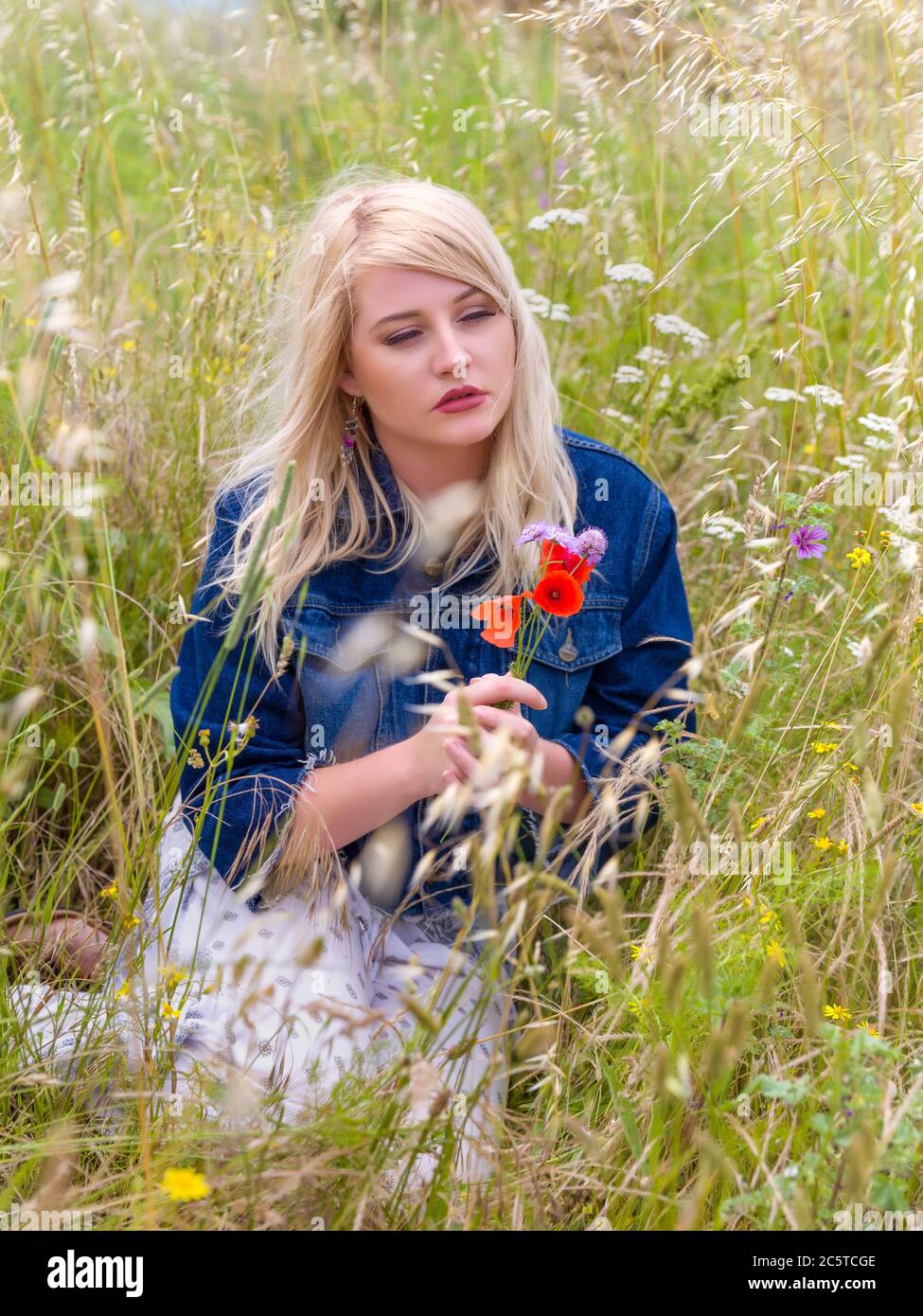 Romantische junge blonde Frau mit roter Mohn Blumen in einem Feld mit hohen Gräsern Stockfoto