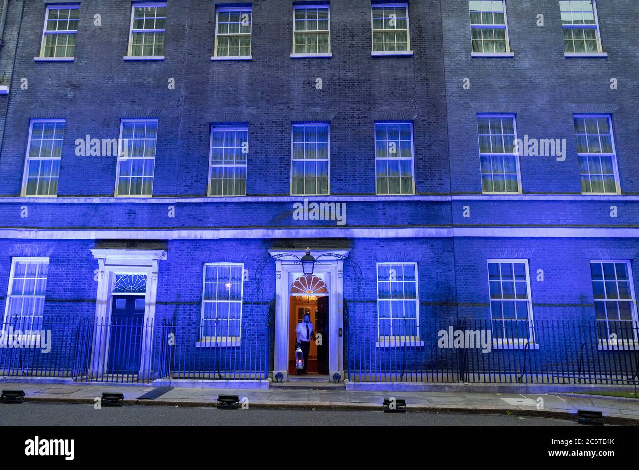 London, Großbritannien. Juli 2020. Ein Mitarbeiter setzt eine Kerze an der Vorderseite der Downing Street, während das Gebäude blau angezündet wird, um den 72. Jahrestag des National Health Service (NHS) in London, Großbritannien am 4. Juli 2020 zu begehen. Laut lokalen Medien wurden Dutzende von Wahrzeichen im ganzen Land blau beleuchtet, um 72 Jahre seit der Gründung des NHS zu markieren. Quelle: Ray Tang/Xinhua/Alamy Live News Stockfoto